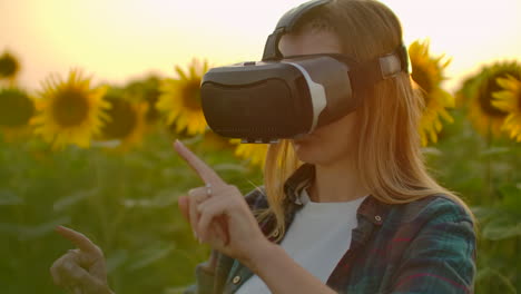 The-female-student-is-working-in-VR-glasses.-She-is-engaged-in-the-working-process.-It-is-a-perfect-sunny-day-in-the-sunflower-field.
